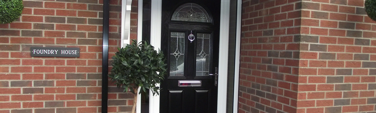 Close up of black composite door with house sign placed on brick wall